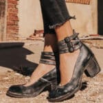 Zwarte leren dameslaarzen met blokhak en dubbele gespsluiting, gedragen met gerafelde jeans. Perfect voor casual en modieuze outfits.