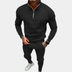 Zwarte herensweater met ritssluiting en bijpassende joggingbroek, gedragen door een man met witte sneakers. Comfortabele sportieve outfit.