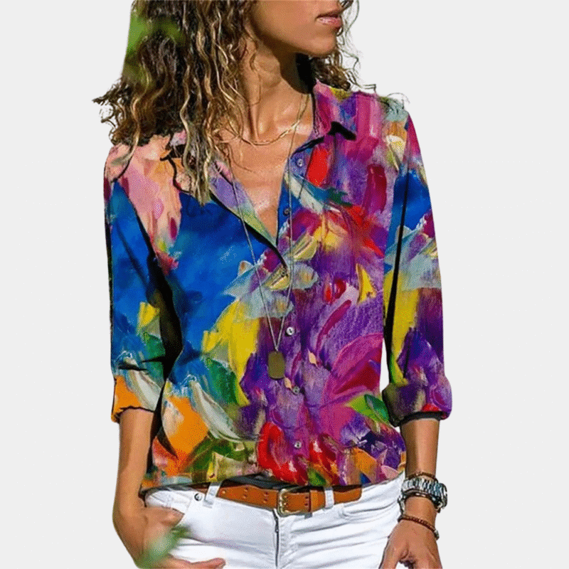 Vrouw in kleurrijke blouse met abstract bloemenpatroon, lange mouwen en kraag, gecombineerd met witte broek. Modieuze dameskleding.