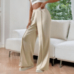 Vrouw in crèmekleurige wijde broek en witte crop top, staand in moderne woonkamer. Trendy damesmode, comfortabele loungewear, stijlvolle outfit.