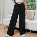 Vrouw in zwarte wijde broek, witte top, witte sokken, moderne woonkamer, houten vloer, comfortabele mode, casual outfit, trendy kledingstijl.