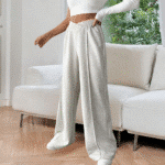 Vrouw in lichtgrijze joggingbroek en witte top in moderne woonkamer. Comfortabele loungewear, trendy mode, casual outfit.
