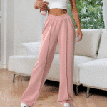 Vrouw in roze wijde broek en wit crop top, staand in moderne woonkamer. Trendy damesmode, comfortabele loungewear, stijlvolle outfit.