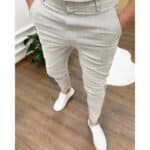 Grijze slim-fit broek voor heren, gedragen met witte sneakers op houten vloer. Stijlvolle casual outfit, ideaal voor moderne mode en comfort.
