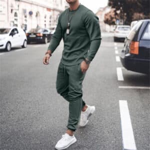 Man in groen trainingspak loopt op straat, draagt witte sneakers en een zilveren ketting. Stijlvolle herenkleding, casual mode, stedelijke achtergrond.