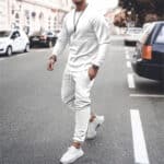 Man in wit trainingspak en sneakers loopt op straat; modieuze sportkleding, casual outfit, stedelijke stijl, comfortabele pasvorm.