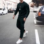 Man in zwart trainingspak en witte sneakers loopt op straat; modieuze herenkleding, casual sportieve outfit, stedelijke stijl.