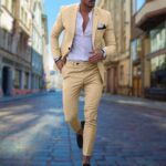 Het beeld toont een man in een stijlvol beige slim fit pak met een witte overhemd en zwarte schoenen, wandelend door een stedelijke straat.