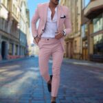 Man in roze slim-fit pak met witte overhemd en zwarte schoenen, wandelend op een geplaveide straat. Stijlvolle herenmode, moderne zakelijke outfit.
