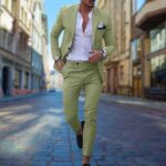 Stijlvolle man in lichtgroen slim fit pak, witte overhemd, zwarte loafers, wandelend in stedelijke straat. Elegante herenmode, moderne zakelijke look.
