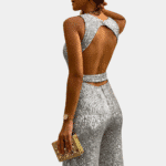Vrouw in zilveren glitter jumpsuit met open rug, elegante avondkleding, houdt gouden clutch. Perfect voor feest of gala. Fashion statement.