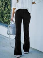 Vrouw in witte kabeltrui met zwarte flared broek en grijze handtas. Modieuze herfstoutfit, casual stijl, straatmode.