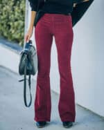 Vrouw draagt bordeauxrode flared broek, gecombineerd met zwarte trui en laarzen, terwijl ze een zwarte handtas vasthoudt. Modieuze herfstoutfit.