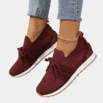 Stijlvolle bordeauxrode damessneakers met gebreid bovenwerk, witte zool en veters, gedragen met blauwe jeans. Perfect voor casual mode en comfort.
